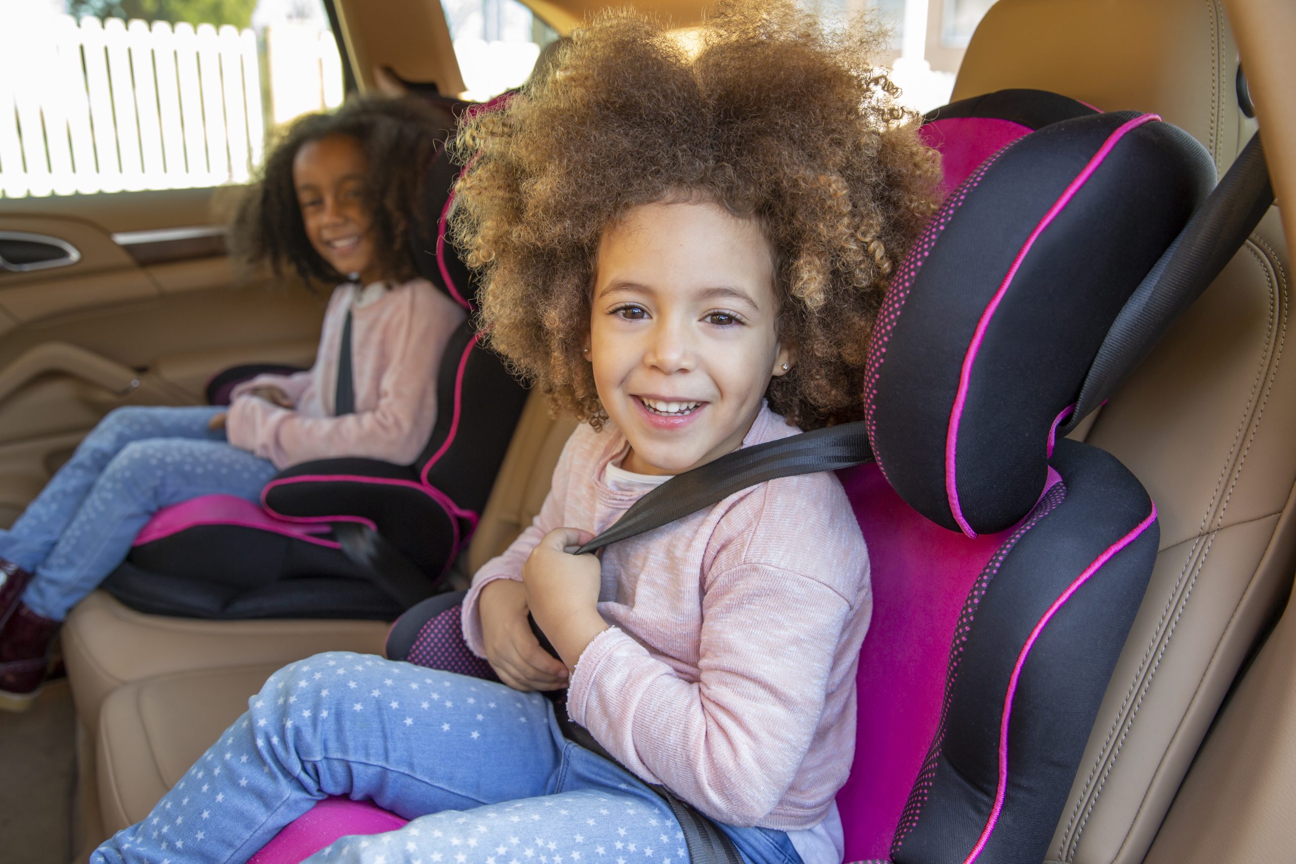 Ethnic kid sister girls in car back seat with safety belts happy smiling