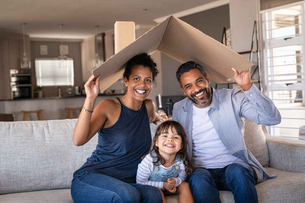 A family holds a piece of cardboard over their heads in their living room, symbolizing the protection offered by home insurance.